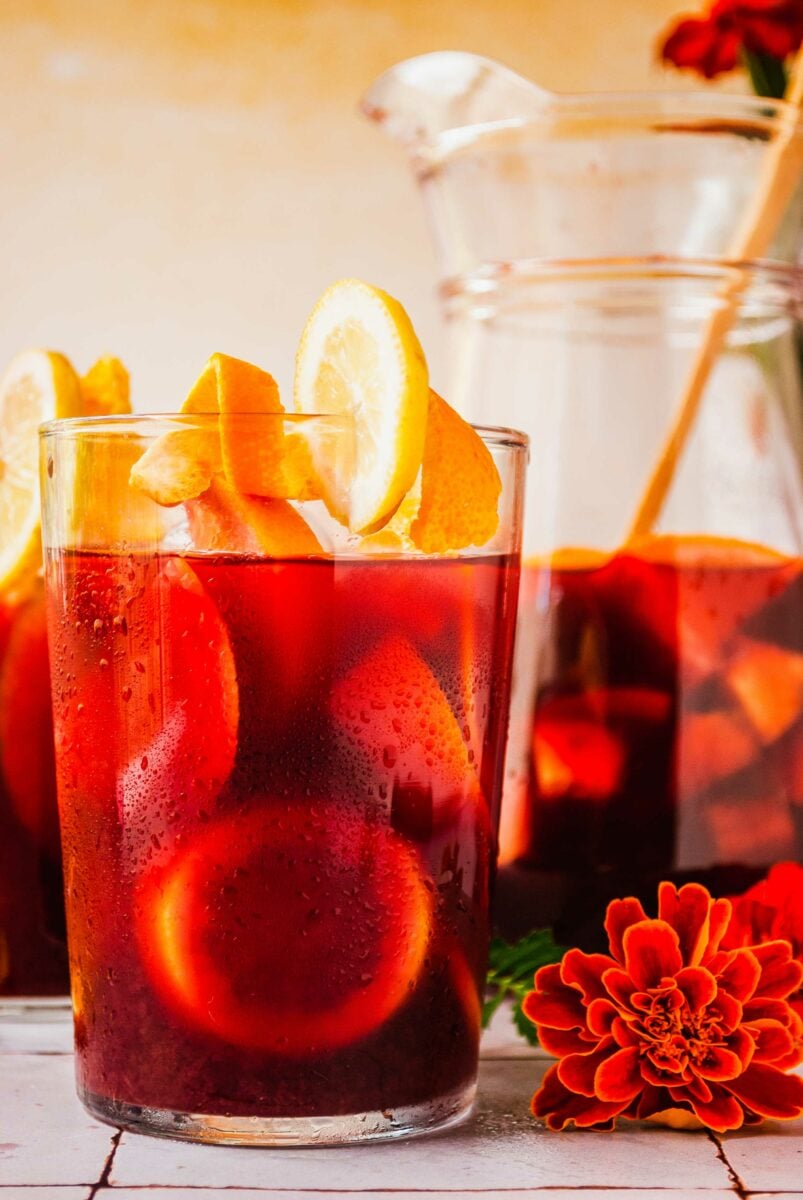 Orange flowers are placed on a tile surface next to a glass of sangria. 