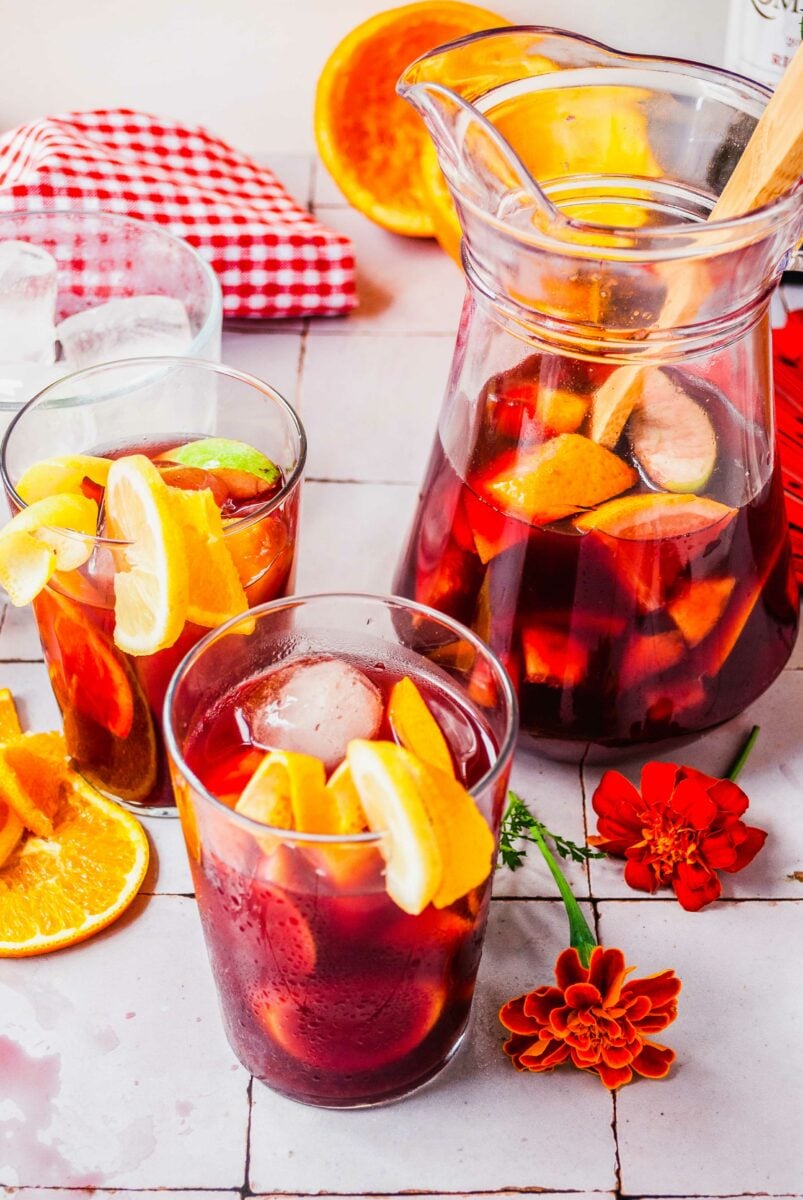 Two glasses of sangria are placed next to a half full pitcher. 