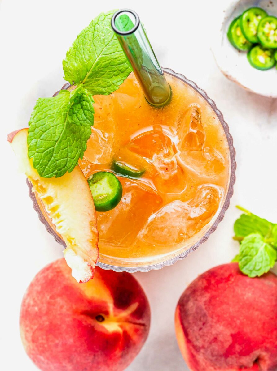 A peach slice and serrano slices sit atop a glass of peach juice. 