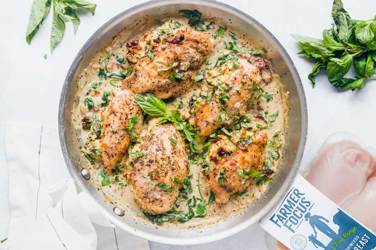 A silver skillet is filled with cooked stuffed chicken breasts in sauce. 