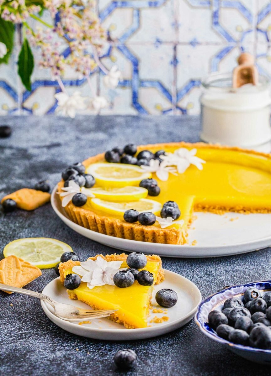 A slice of lemon tart is presented on a white plate. 