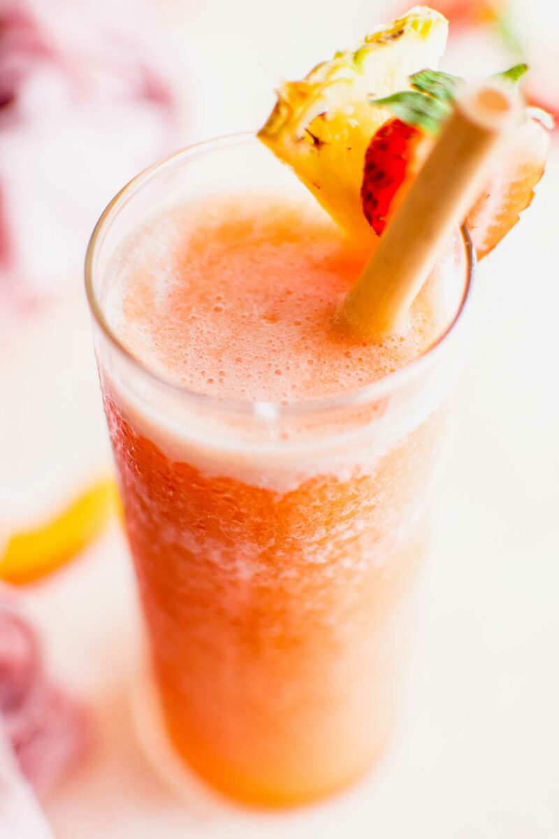 A glass is garnished with fresh fruit and filled with slushy. 