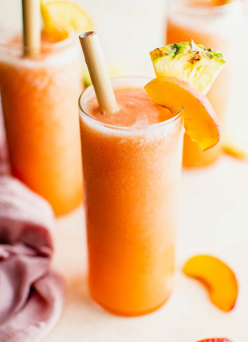 A glass filled with orange slushy is topped with fresh fruit. 