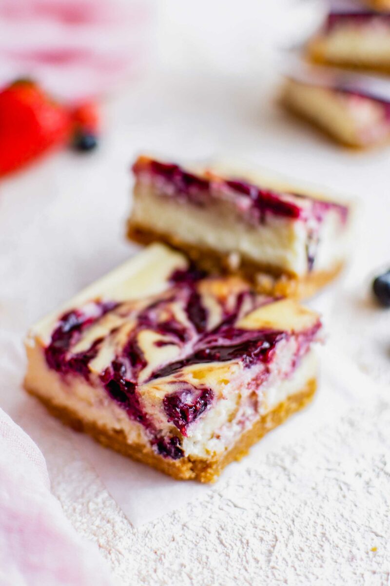 A berry swirled cheesecake bar is on a tiny sheet of parchment paper. 