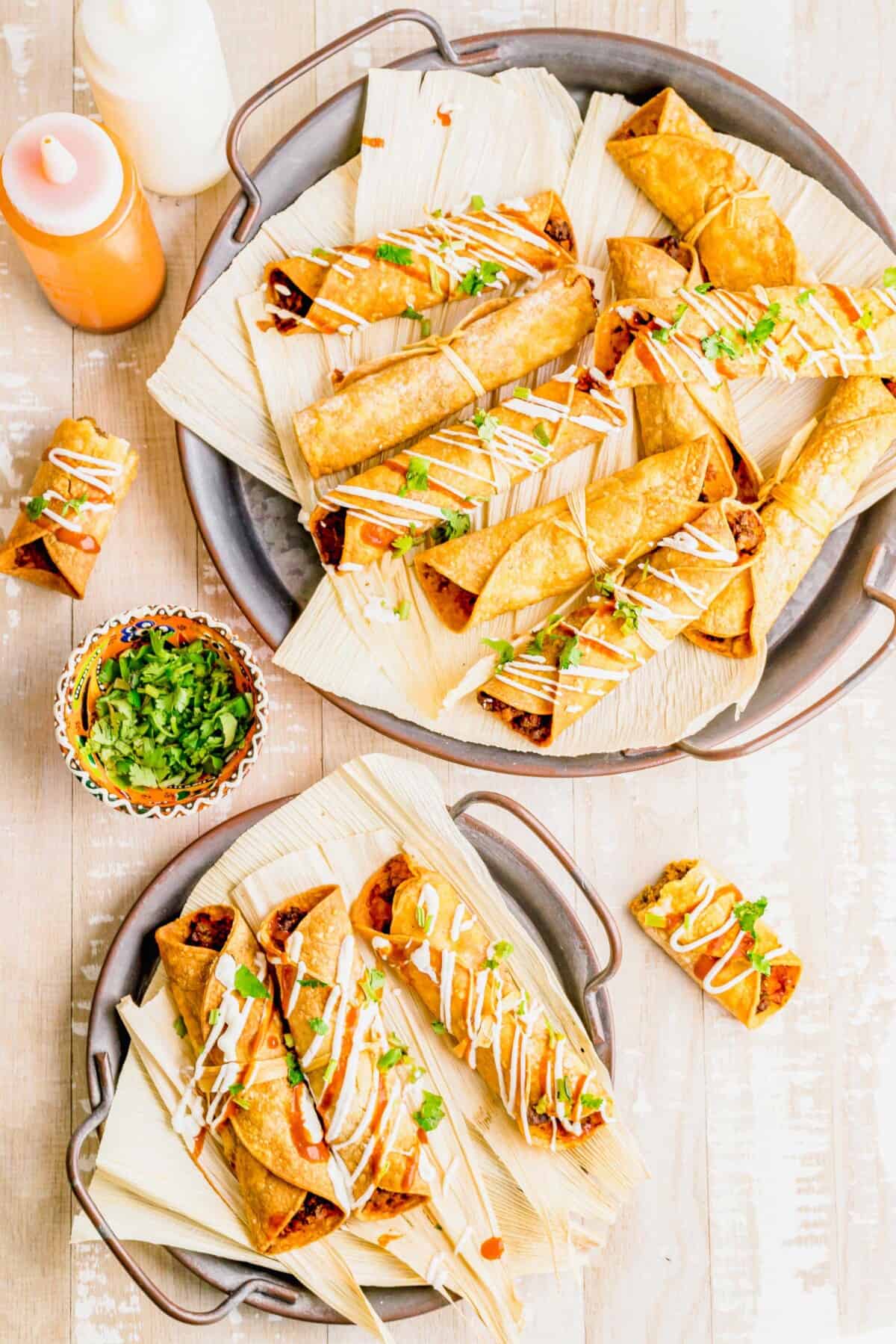 air fried beef taquitos lay on corn husks next to a fresh bowl of cilantro