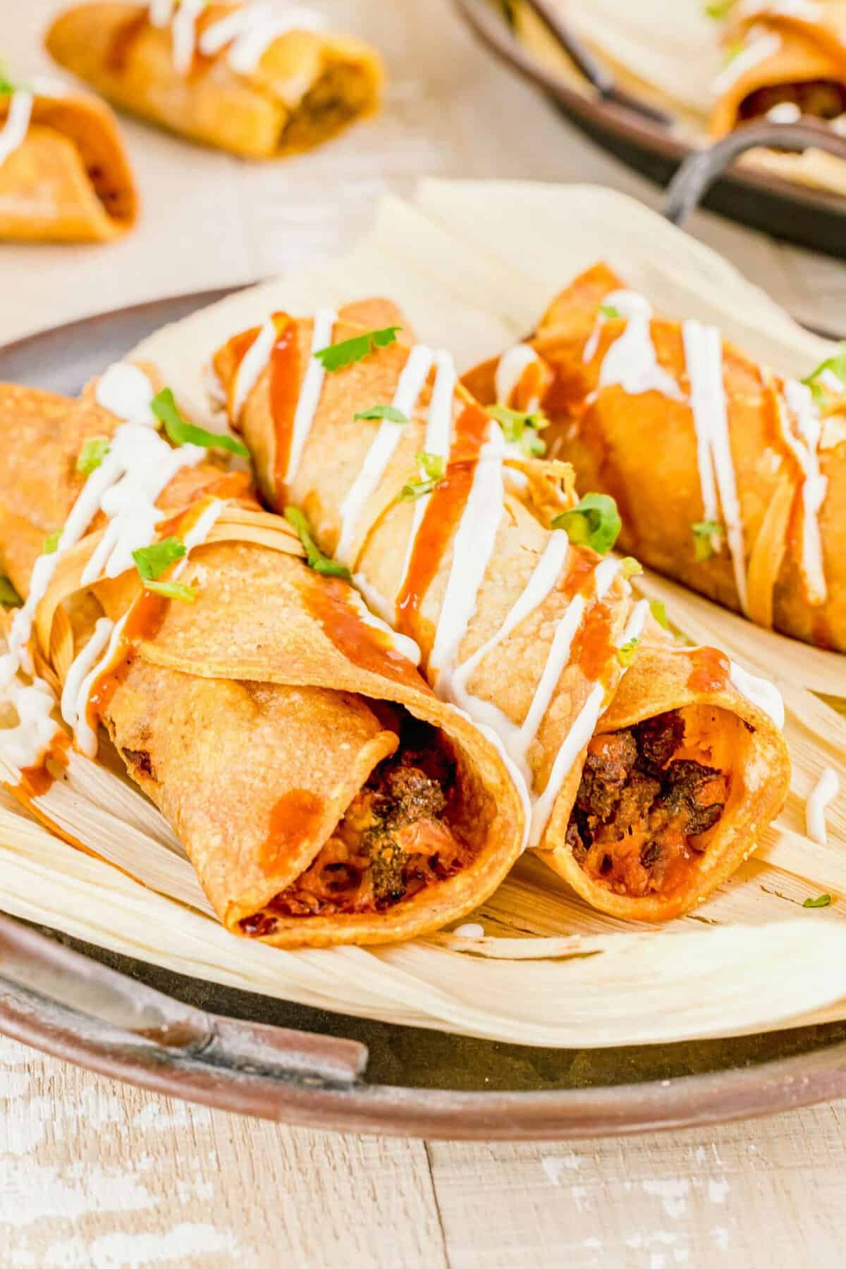 Several air fried taquitos are placed on corn husks. 