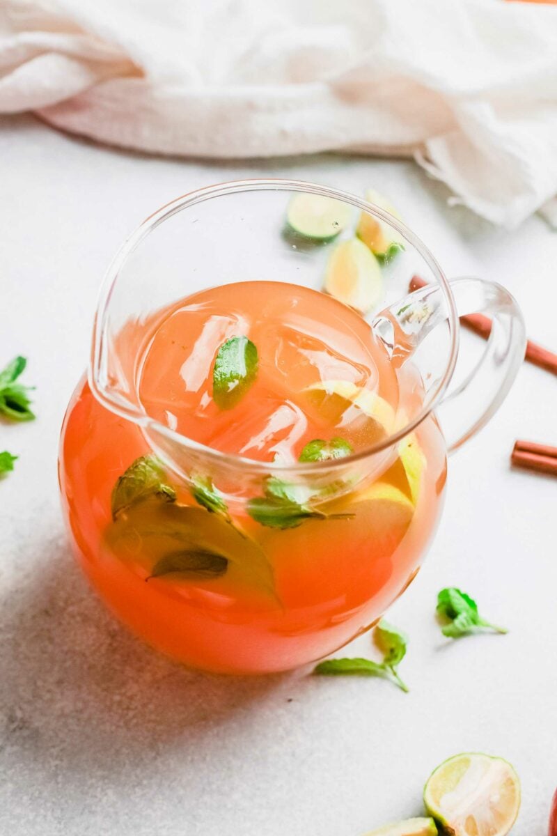 A pitcher of apple cider mojito is placed on a white surface.