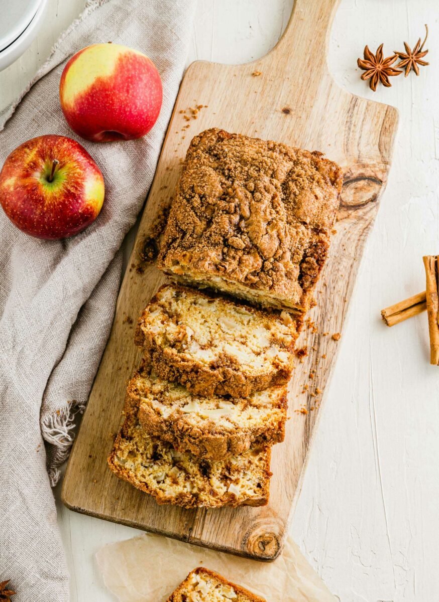 A loaf of apple cinnamon swirl bread is being sliced on a wooden cutting board. 