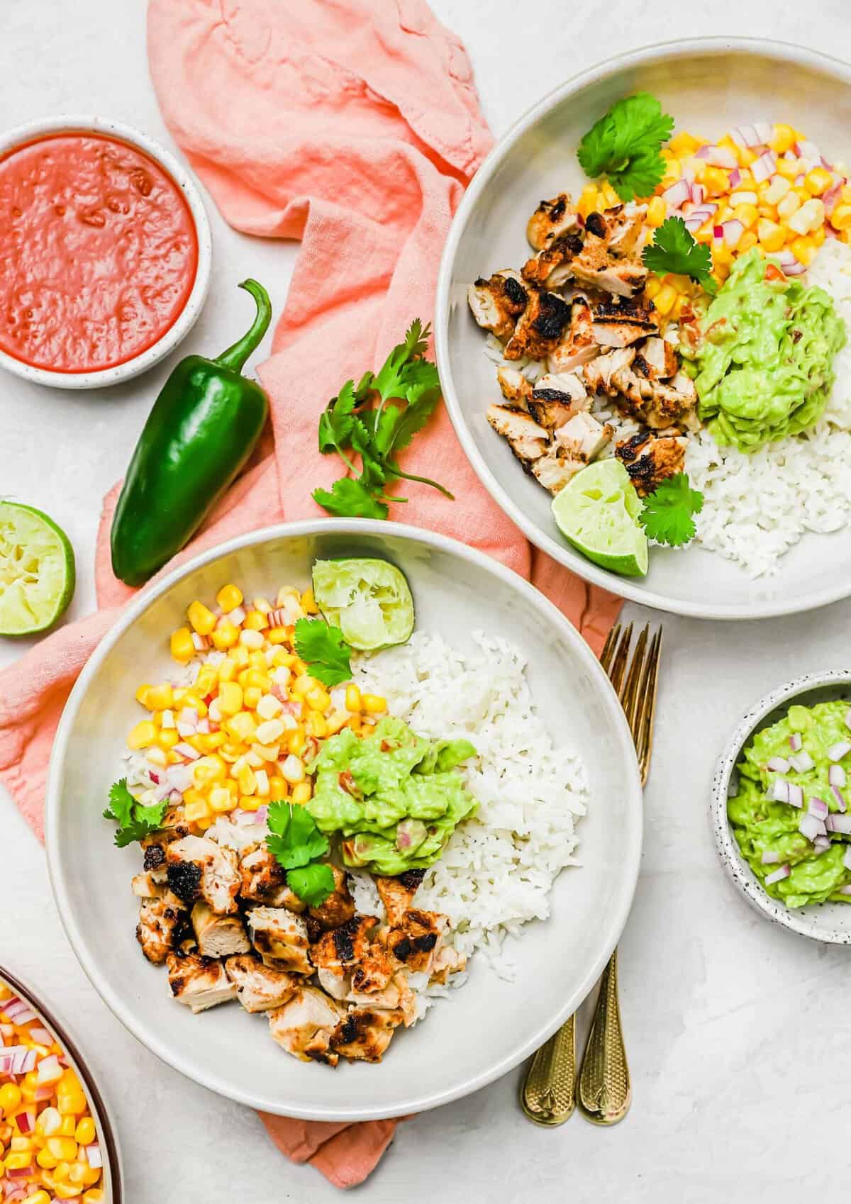 Overhead view of two chicken burrito bowls surrounded by bowls of toppings