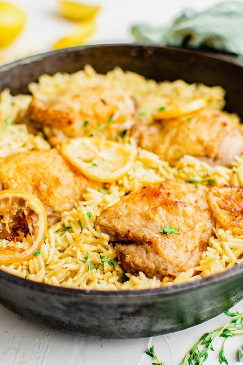 A pan is filled to the brim with cooked orzo, chicken, and lemon slices. 