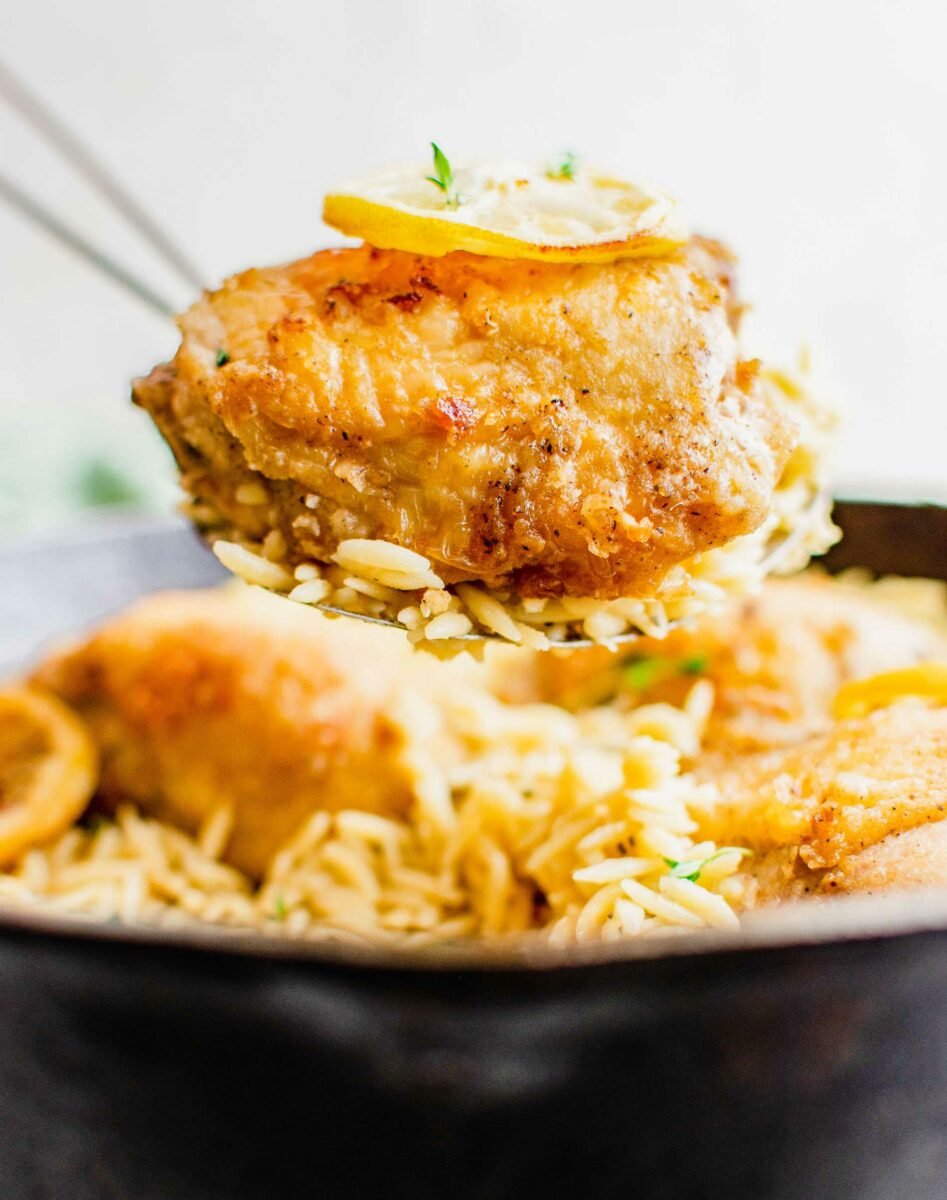 A piece of chicken is being lifted with some orzo from the pan. 