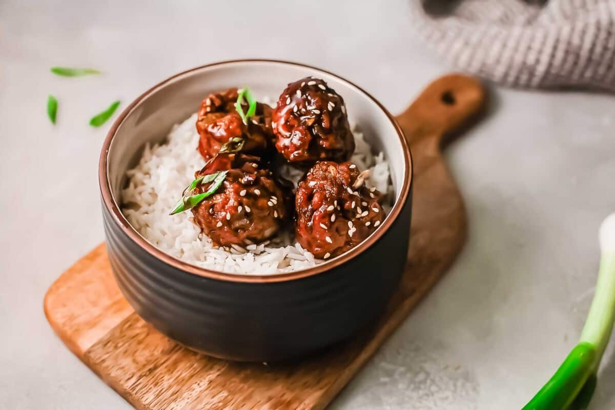 Meatballs in white rice in a bowl are placed on a wooden cutting board. 