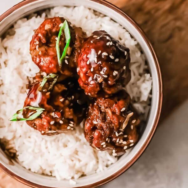 4 mongolian meatballs on a bed of white rice in a bowl on a wooden cutting board