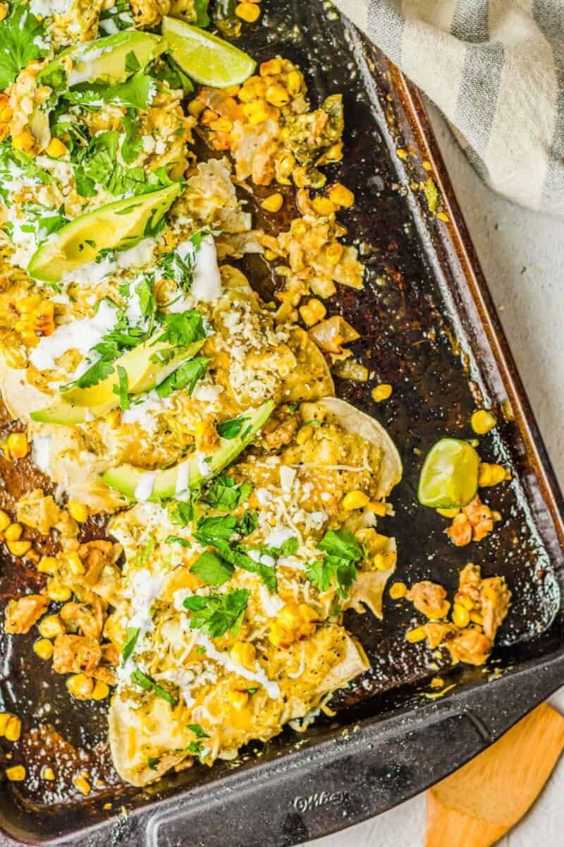 A batch of chicken enchiladas are fully baked and garnished on a black sheet pan.
