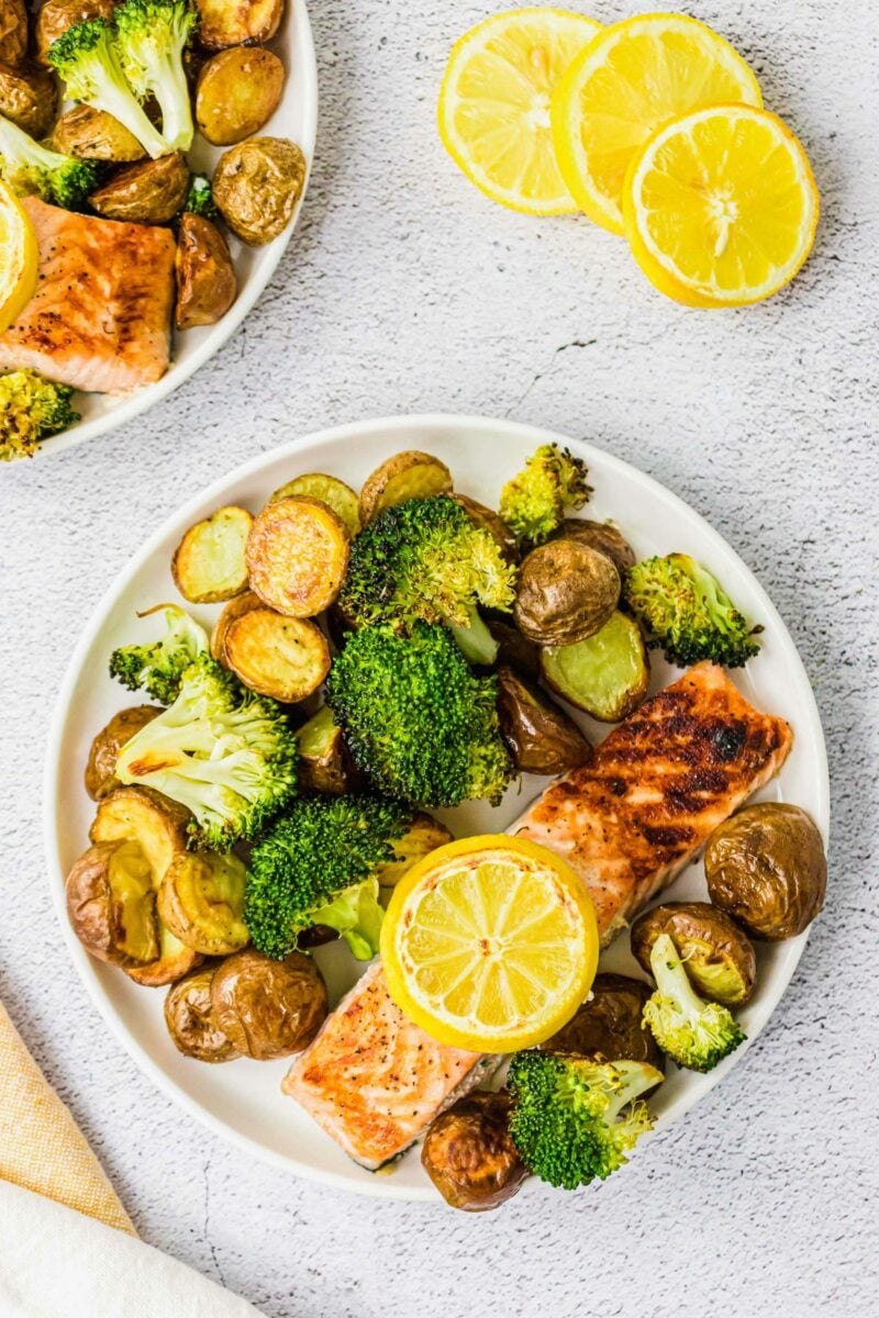 A white plate is filled with a salmon filet, potatoes and broccoli. 