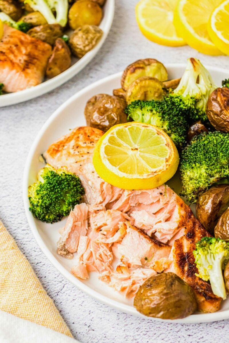 A salmon filet has been broken apart by a fork on a white plate. 