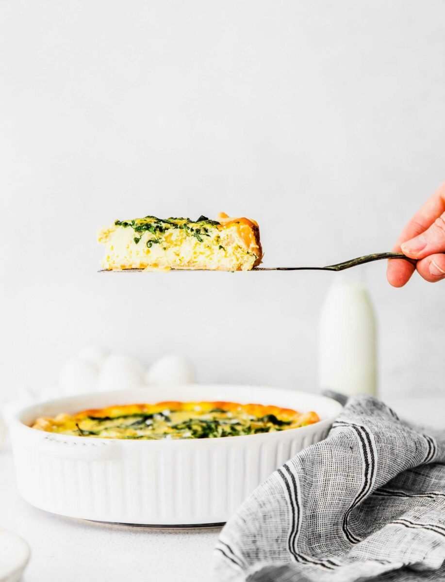 A slice of quiche is being lifted with a serving utensil from the rest of the dish.