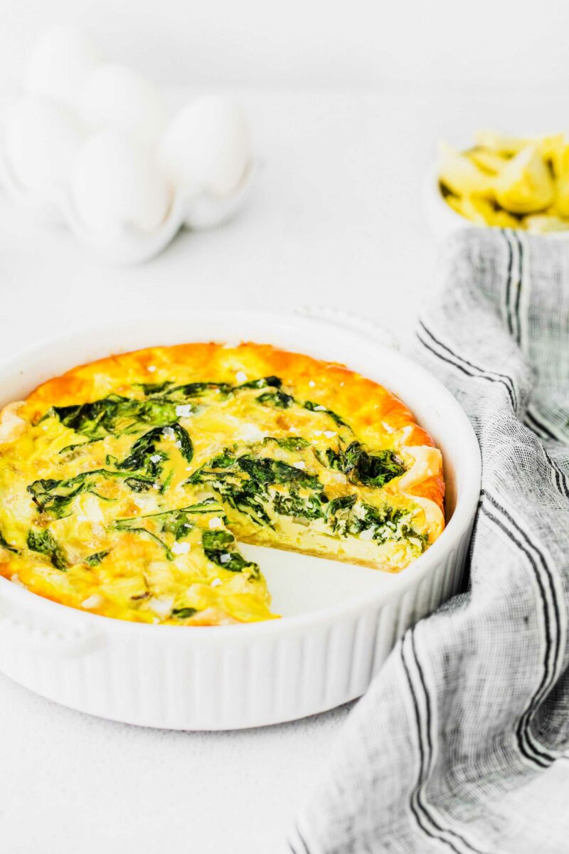A slice of quiche is missing from a white pan. 