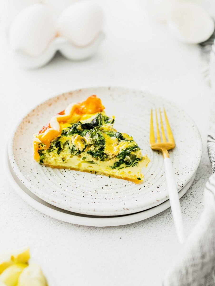 A fork is placed on a white plate that has a single slice of quiche on it. 