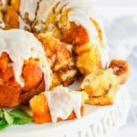 several pieces of apple monkey bread are pulled away from the monkey bread on a white cake platter
