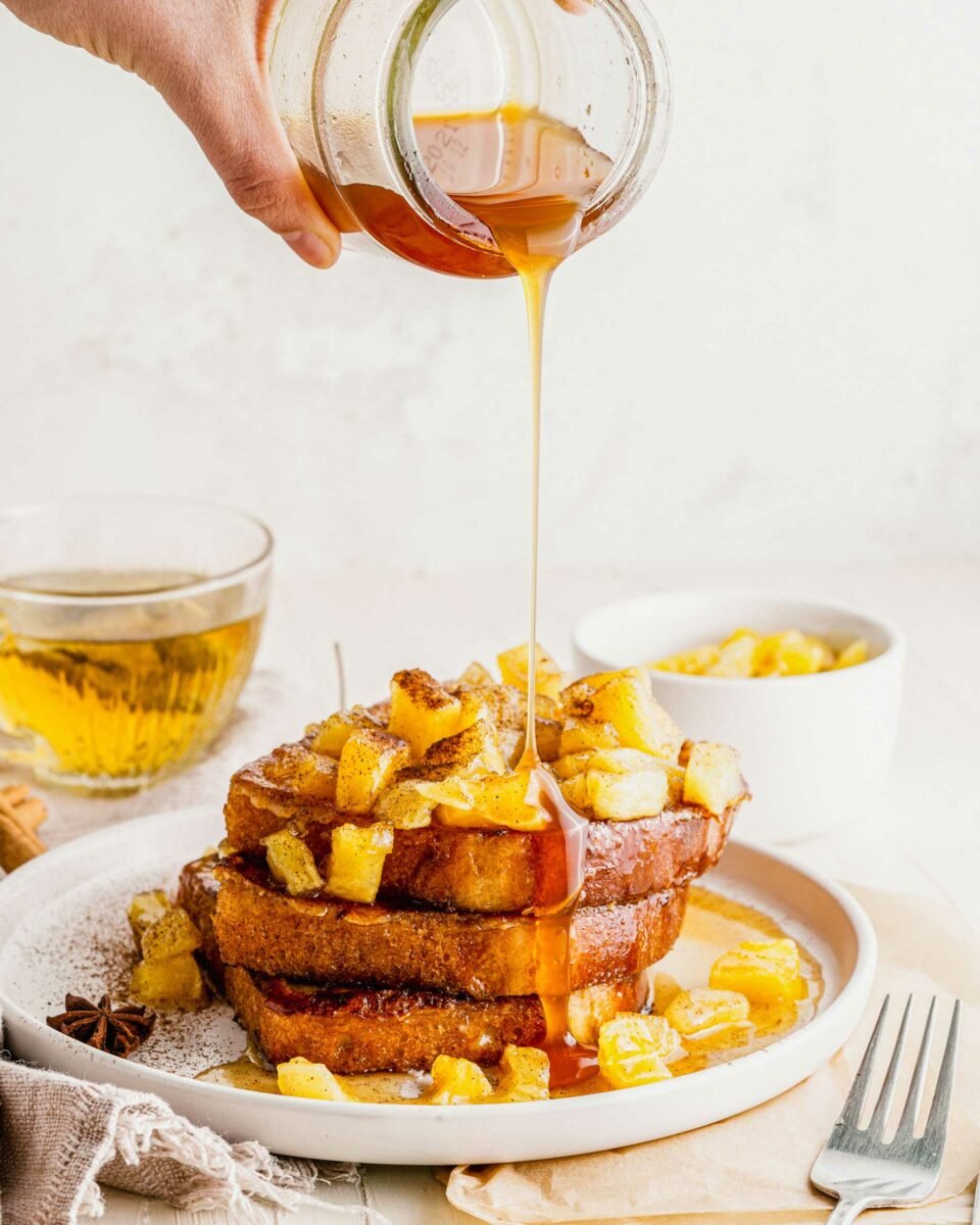 Syrup is being drizzled on top of the French toast and apples. 