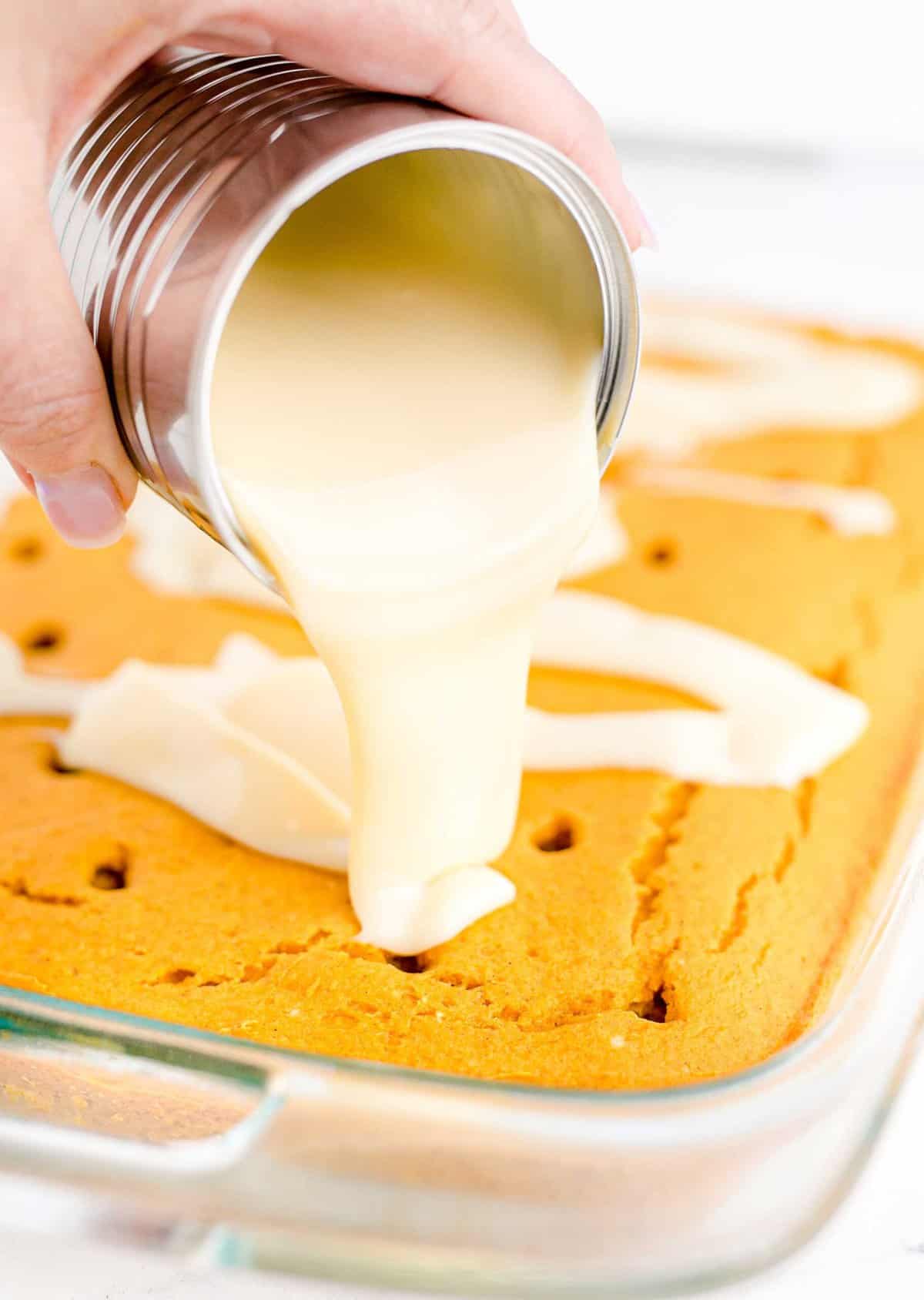 Pouring cream over a pumpkin cake with holes poked into it