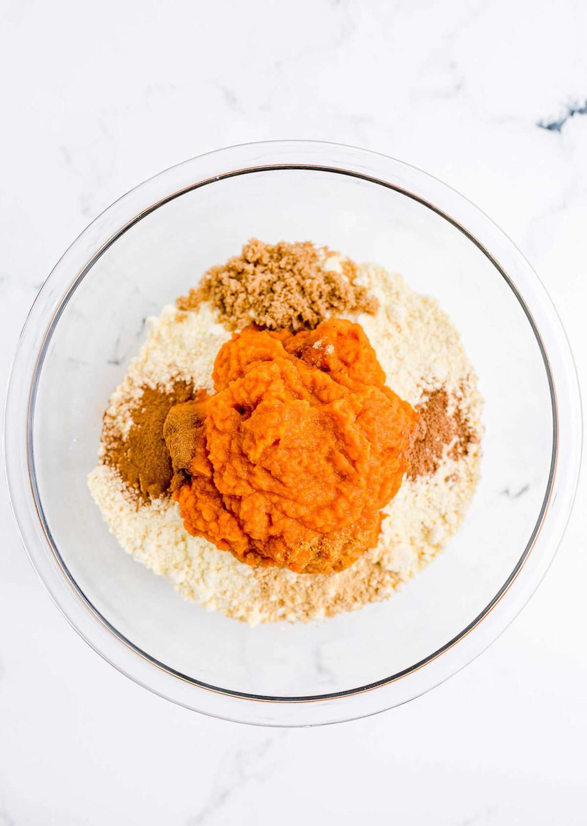 A glass mixing bowl with flour, pumpkin and other cake ingredients