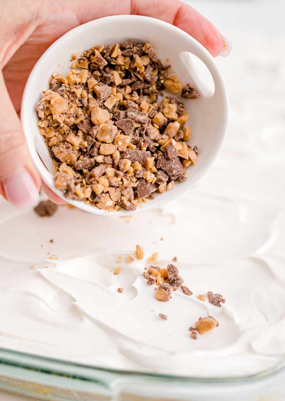 Pouring toffee bits onto a frosted cake