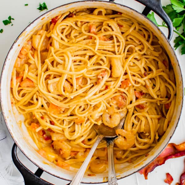 cajun shrimp pasta is in a large pot with a metal serving fork and spoon next to fresh parsley