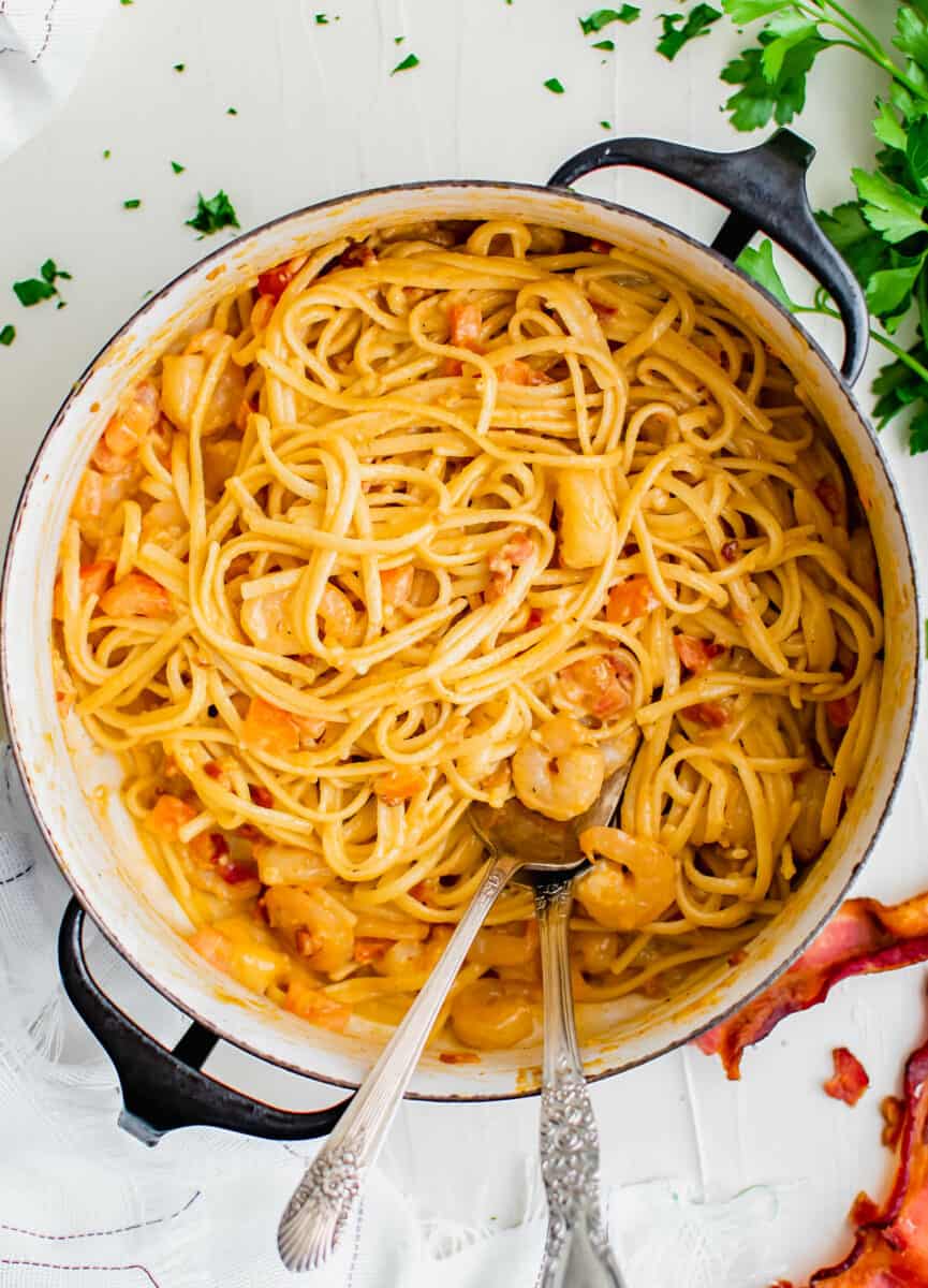 Two spoons are placed in a large pot filled with creamy shrimp pasta.