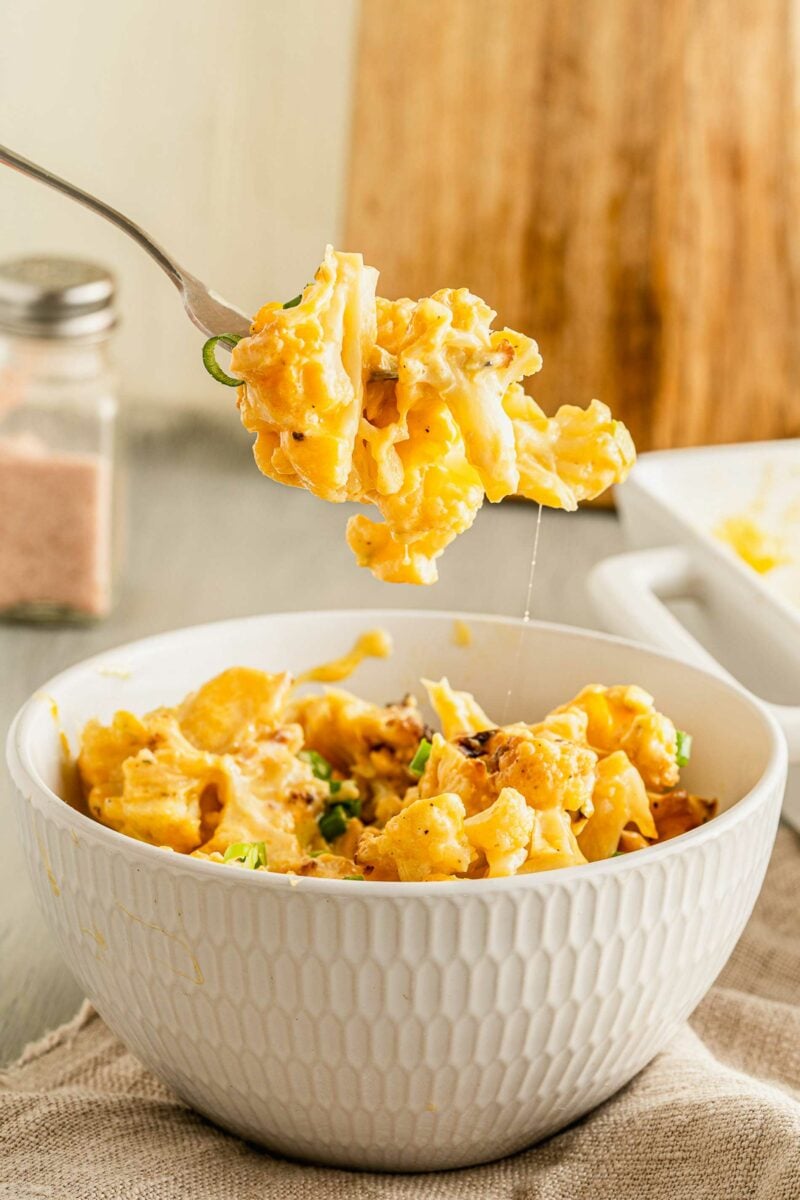 A fork is lifting a bite of cauliflower from a white bowl. 