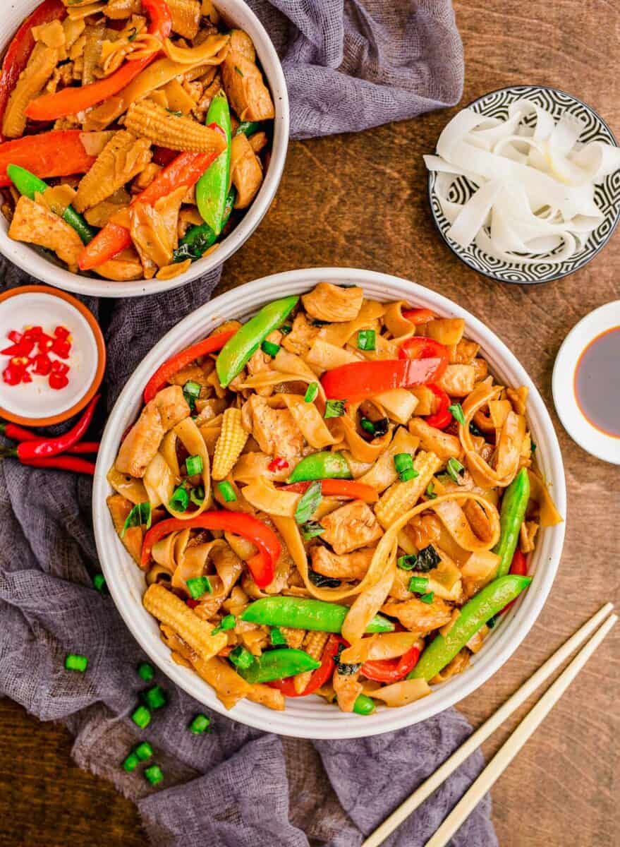 Chopsticks are placed next to a bowl of drunken noodles with chicken. 