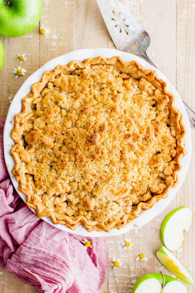 A dutch apple pie is presented in a white baking dish. 