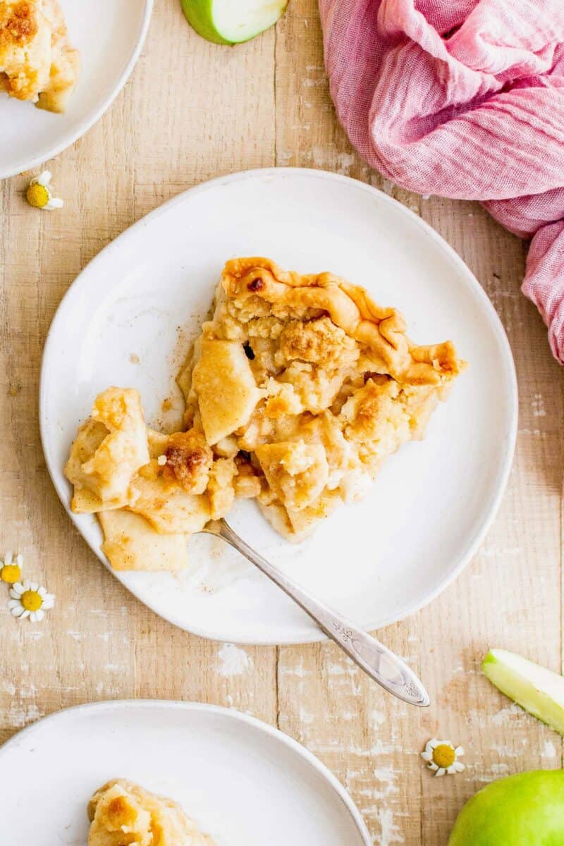 A fork is digging into a slice of homemade dutch apple pie that's placed on a white plate. 