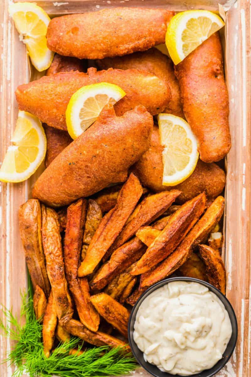 Fried fish is served with lemon slices and fries with a side of tartar sauce. 