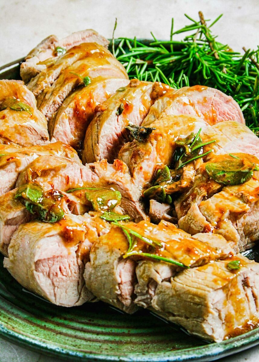 A sliced pork tenderloin is topped with fresh herbs and glaze. 