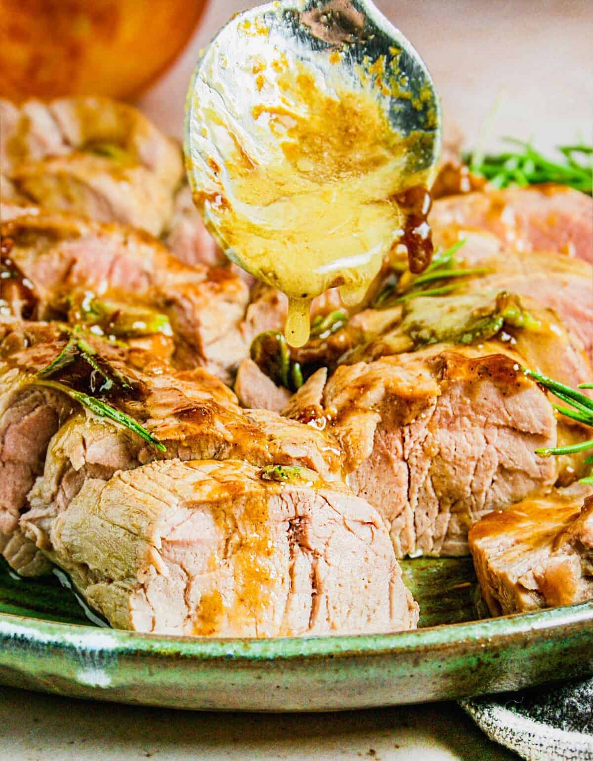 A spoon is drizzling golden brown glaze on a piece of pork.