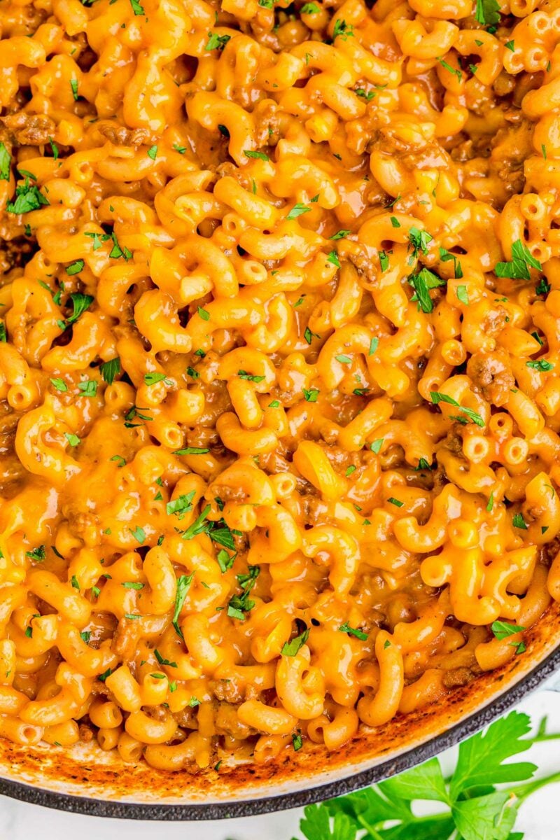 Cheesy noodles and ground beef are garnished with fresh parsley. 