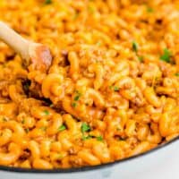 a wooden spoon scoops up cheesy pasta from a cast iron skillet