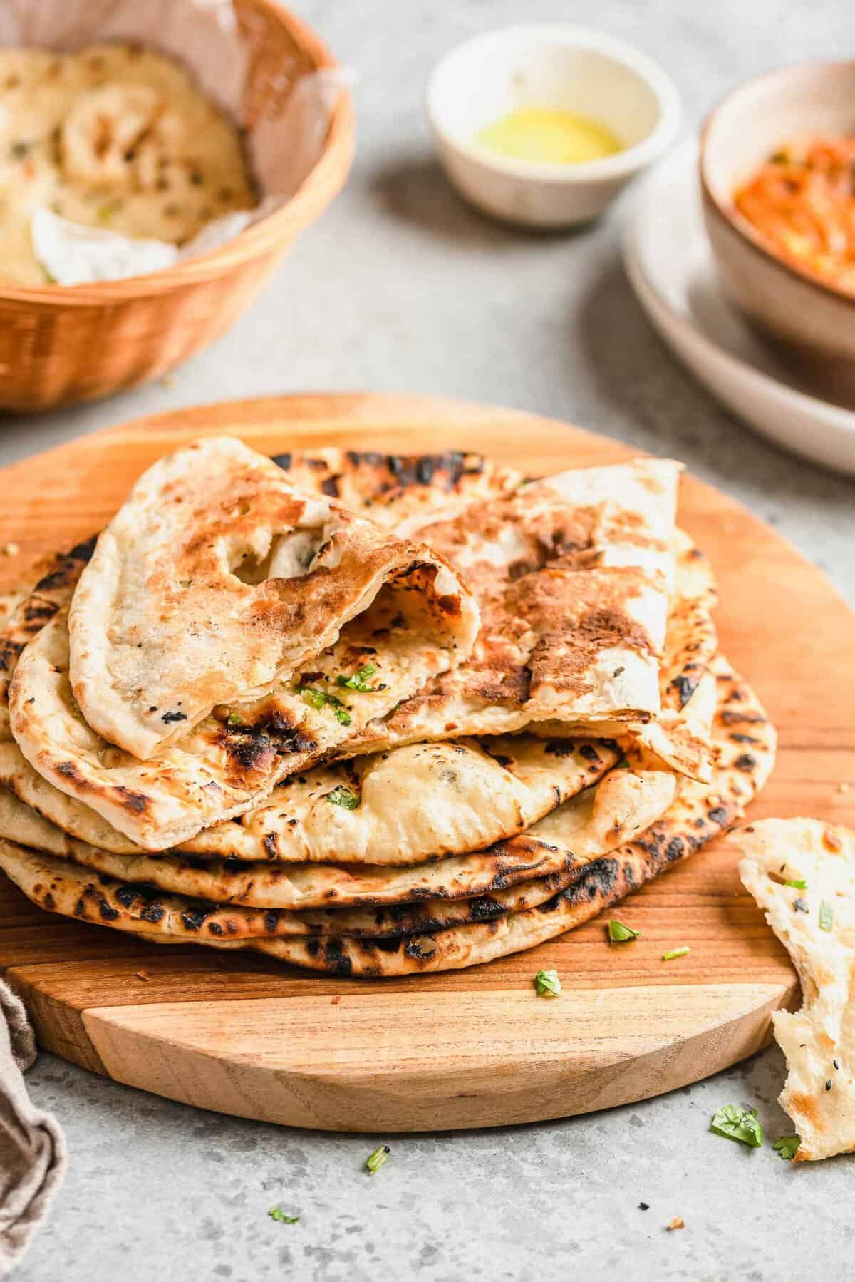 Round pieces of naan are in a stack on a wooden surface. 