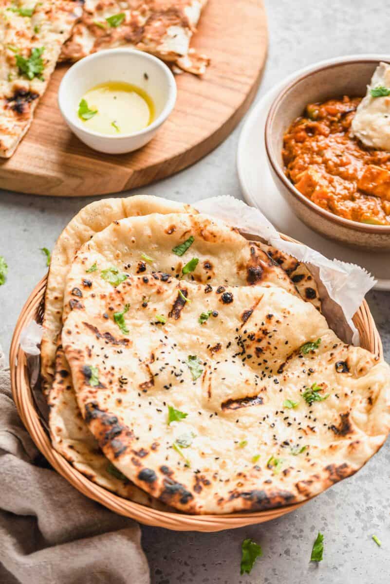 Pieces of naan are placed on top of one another in a wicker basket. 