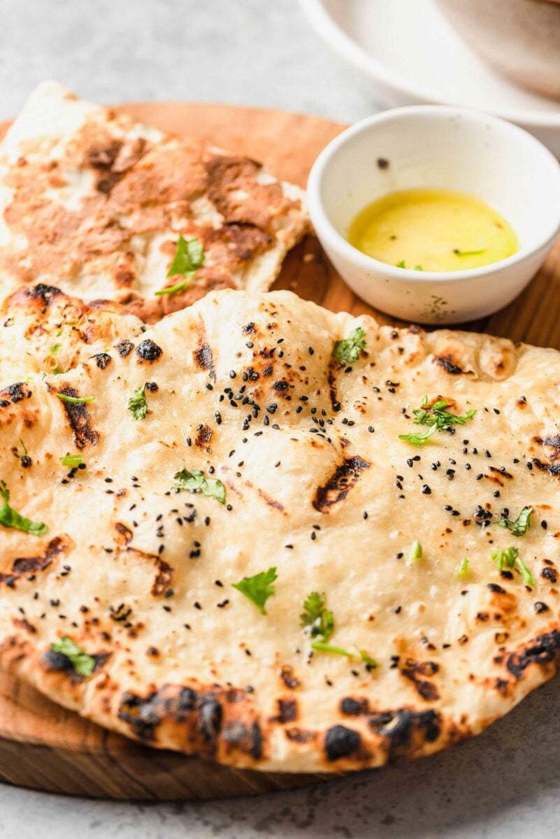 Black seeds and shredded green herbs are spread across freshly baked naan. 