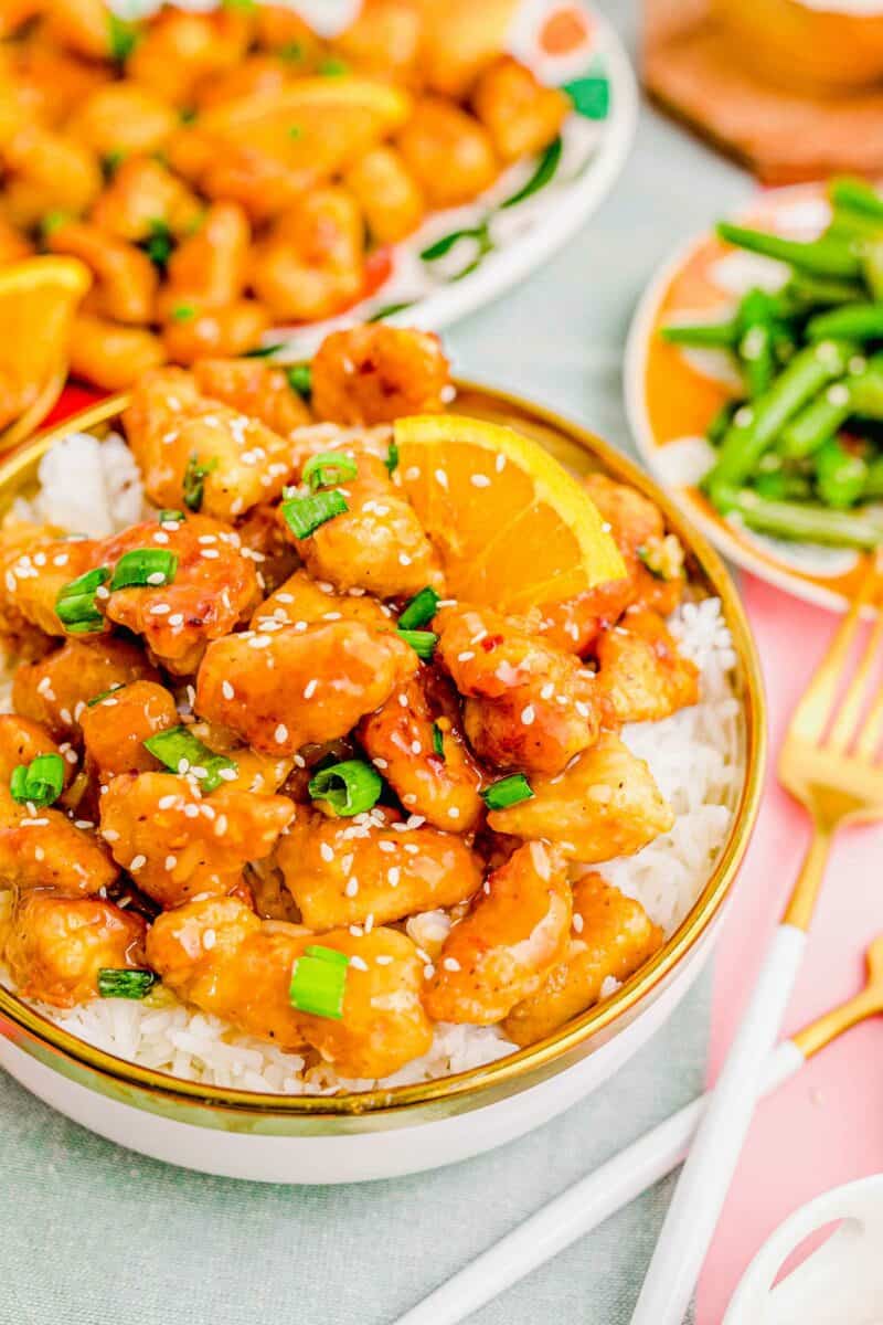 A fork is placed next to a serving of orange chicken and rice. 