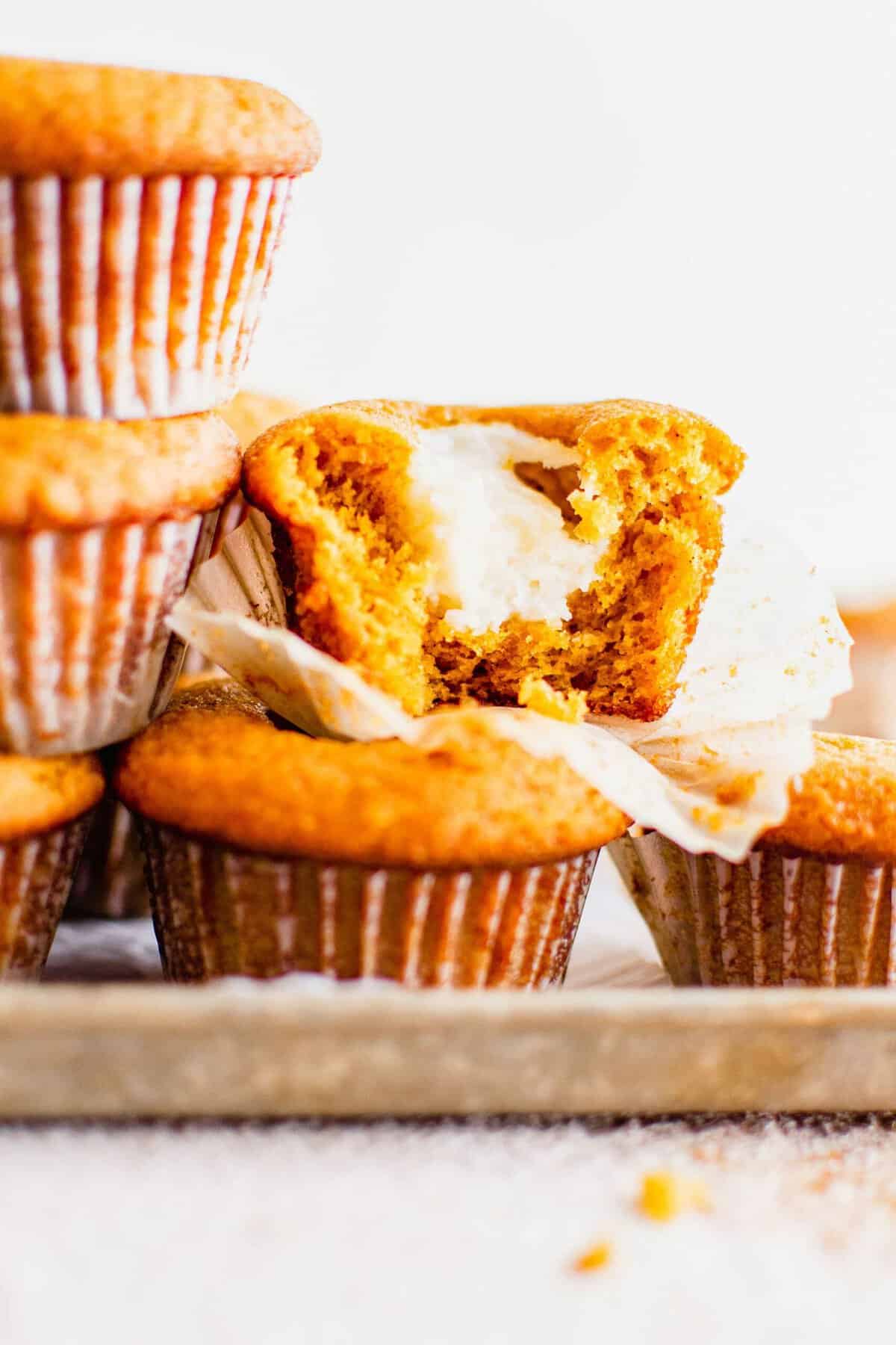 A pumpkin muffin is cut in half, revealing a white cream cheese center. 