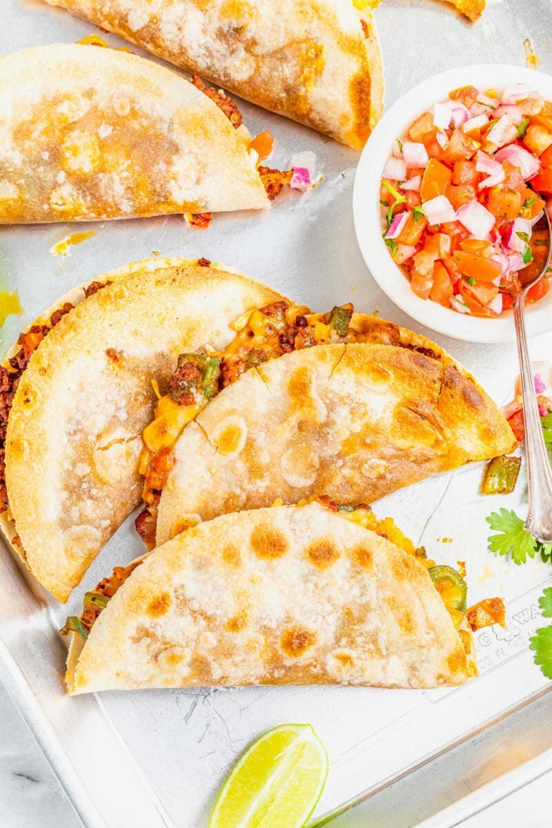 A small bowl of pico de Gallo is placed next to several quesadillas.