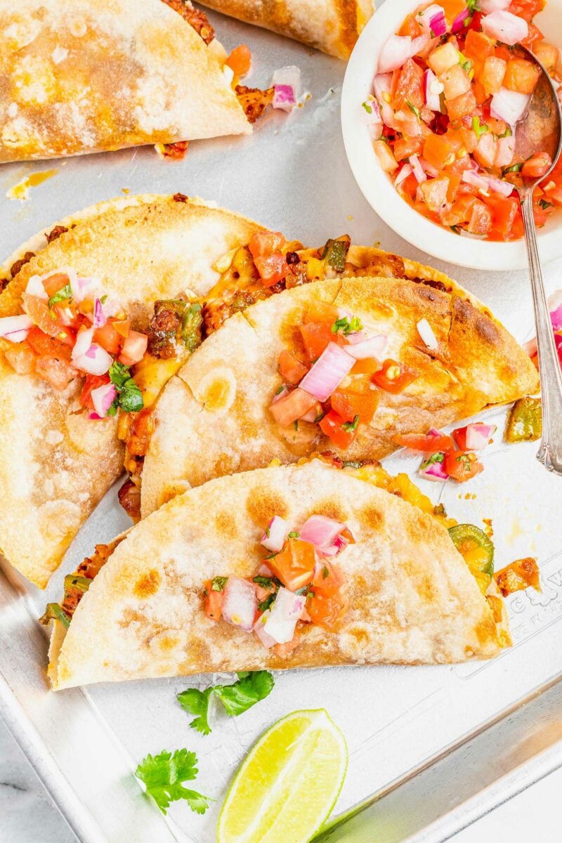 Several quesadillas are placed on a white surface and topped with pico de Gallo. 