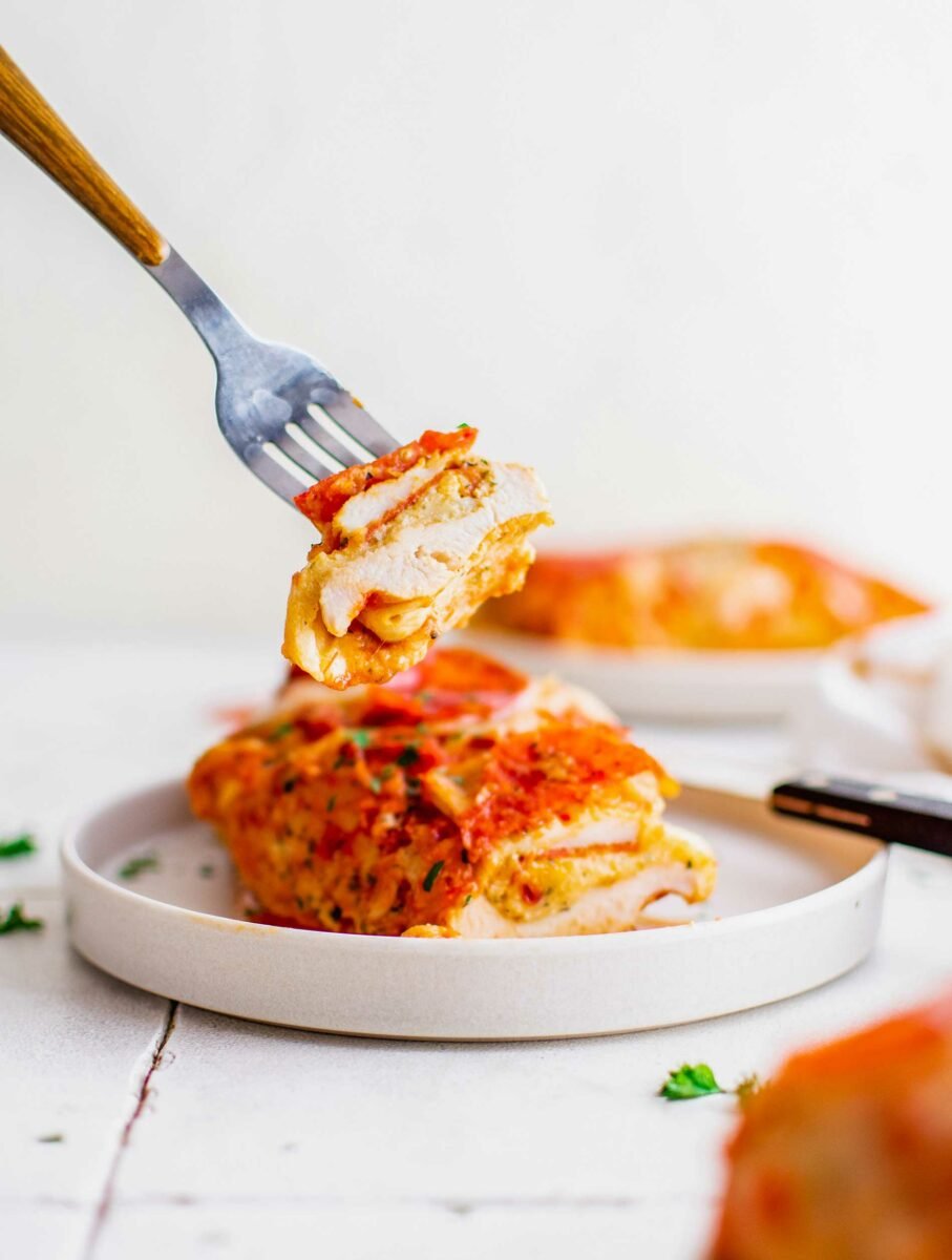 A bite of pizza stuffed chicken is being lifted from a white plate. 