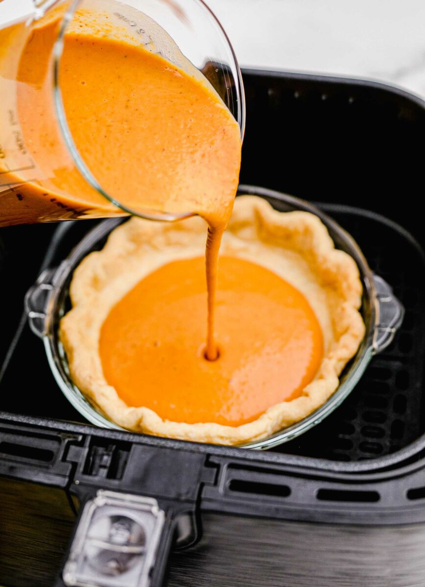 Pumpkin pie batter is being poured into a baked pie crust.