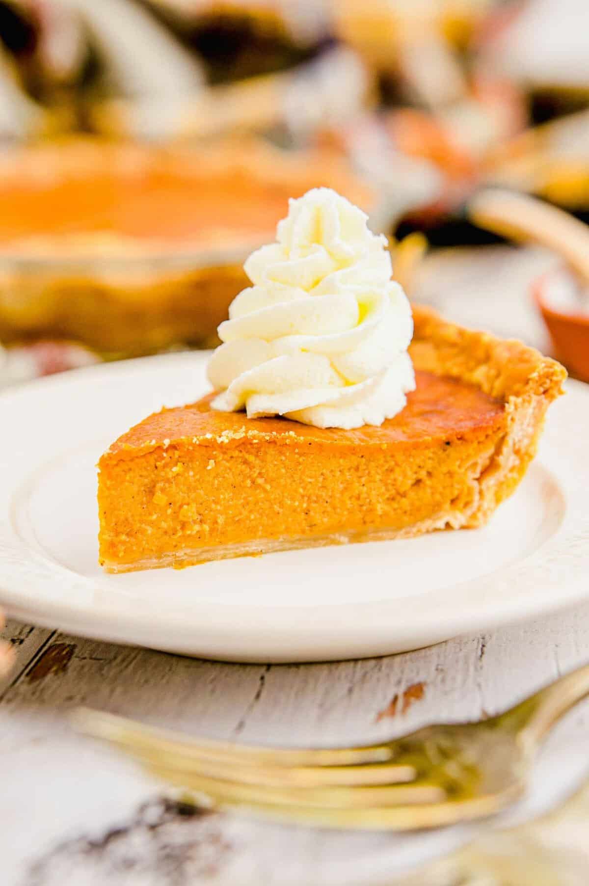 A swirl of fluffy white whipped cream is on top of a slice of pumpkin pie.