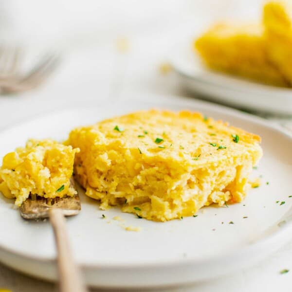 A slice of cornbread casserole on a plate with a bite taken out of it.